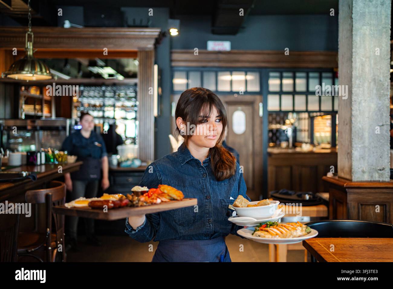 Waitress serving multiple food plates in restaurant Stock Photo
