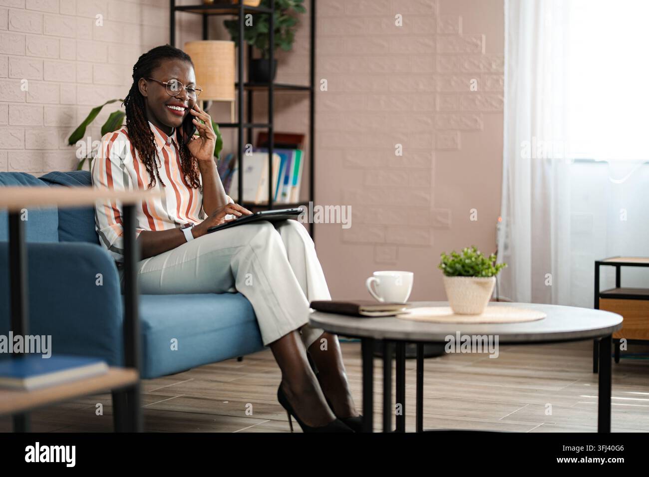 Smiling black woman having a phone call while using a tablet for remote work Stock Photo
