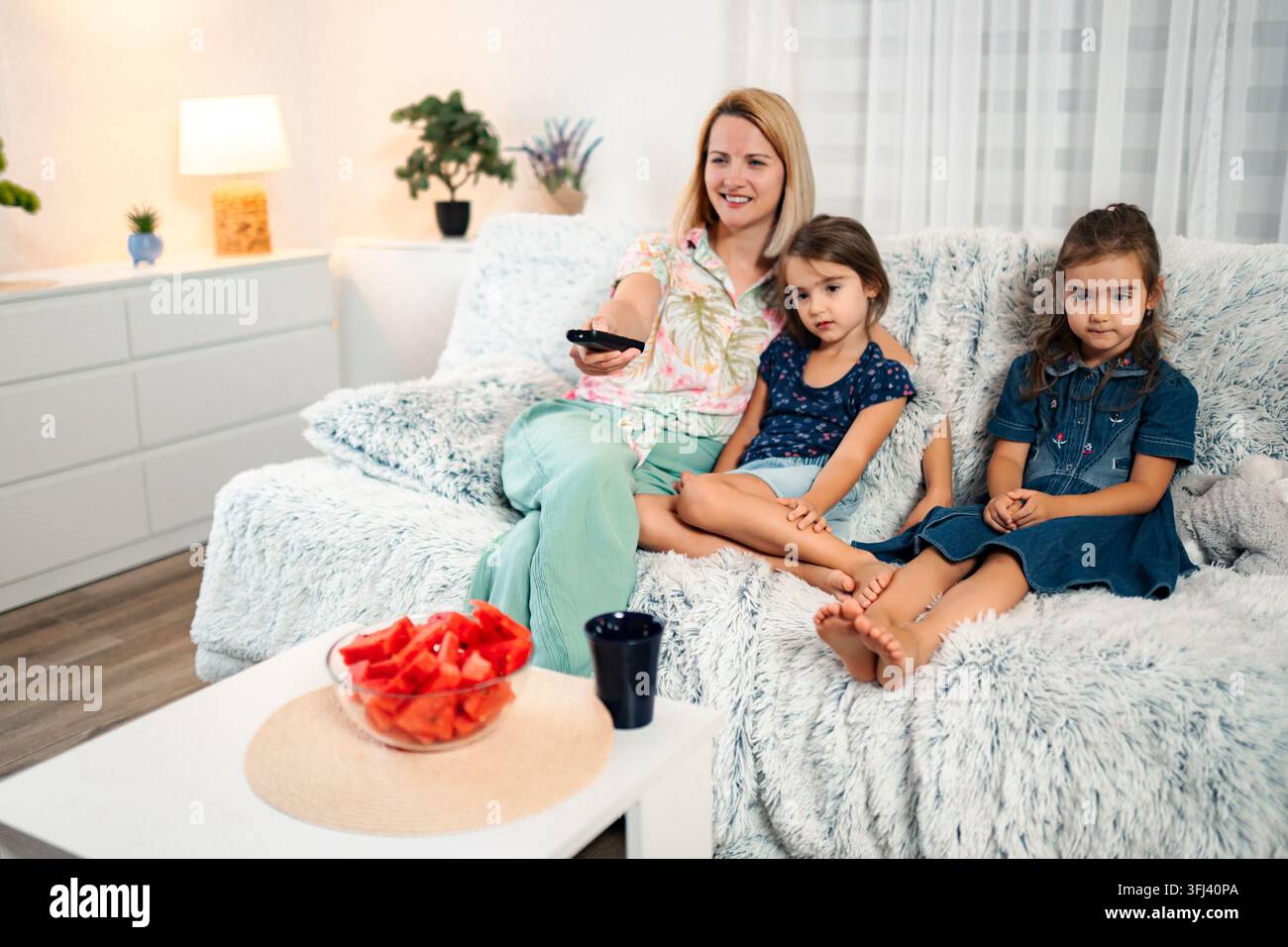 Mother and daughters watching TV relaxing together on couch Stock Photo