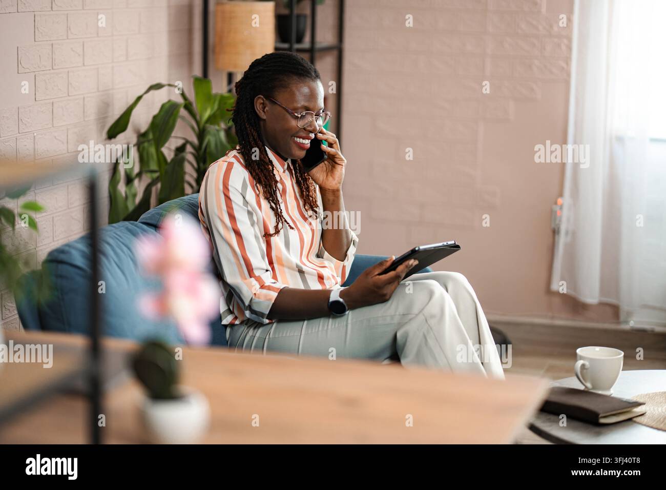 Young black woman sitting on sofa using tablet and smartphone Stock Photo