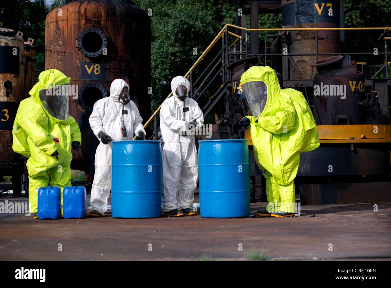 Four workers in chemical protective suits handle blue barrels during hazardous material emergency training Stock Photo
