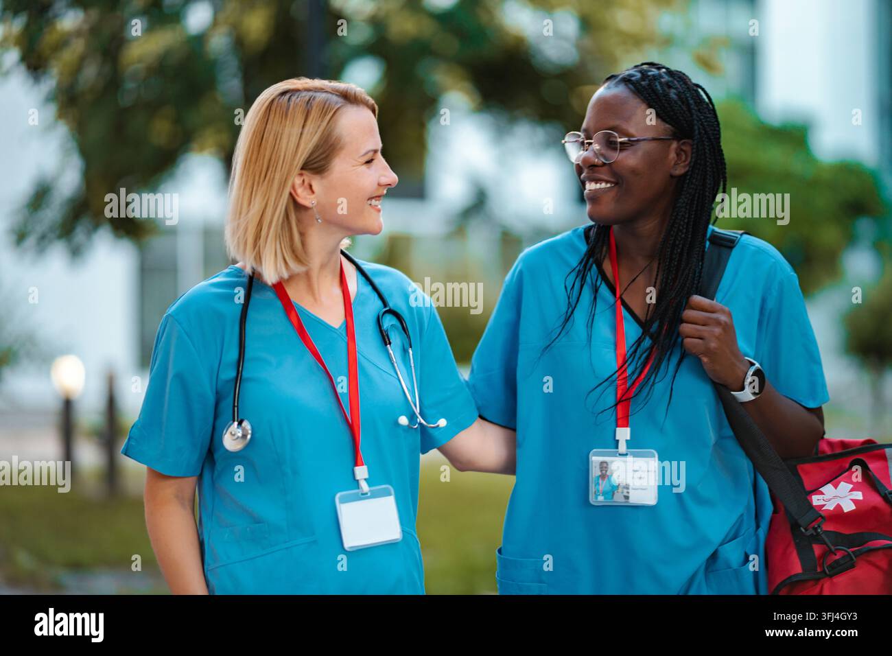 Diverse nurses smiling while walking together, discussing work outdoors Stock Photo