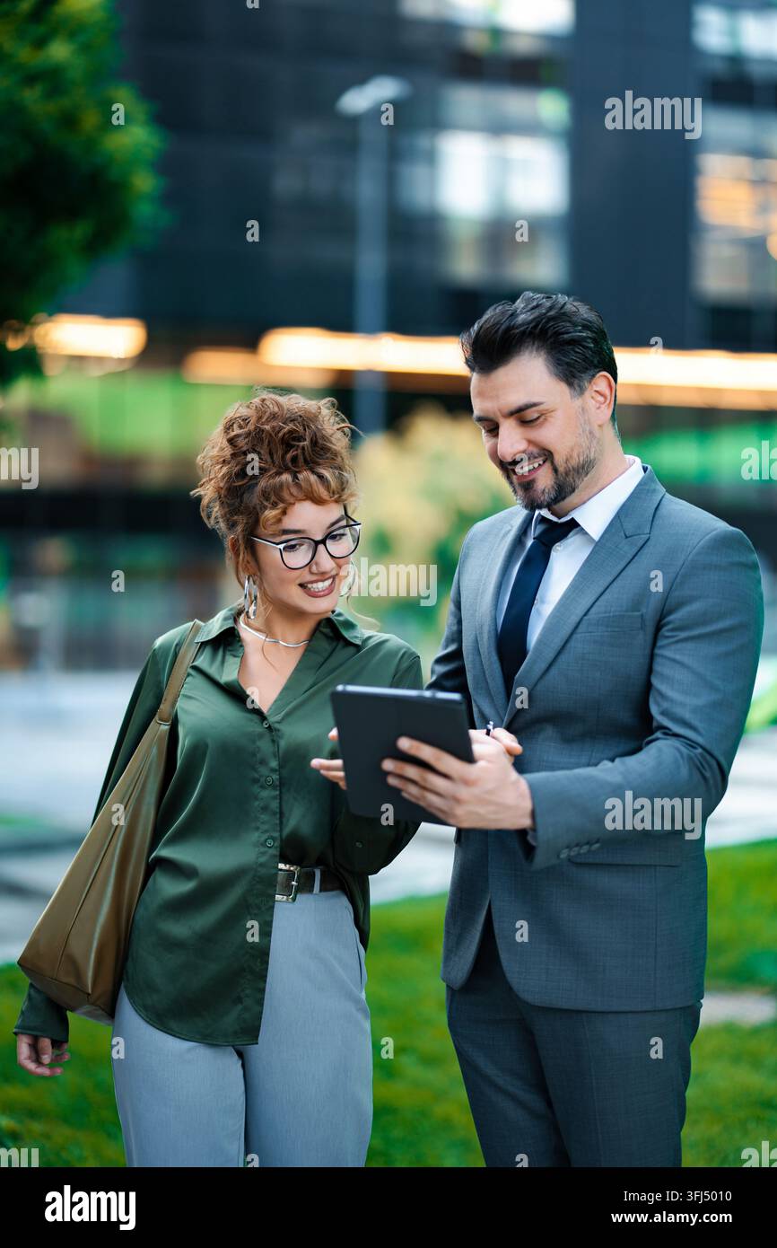 Business professionals collaborating outdoors, using digital tablet for work Stock Photo