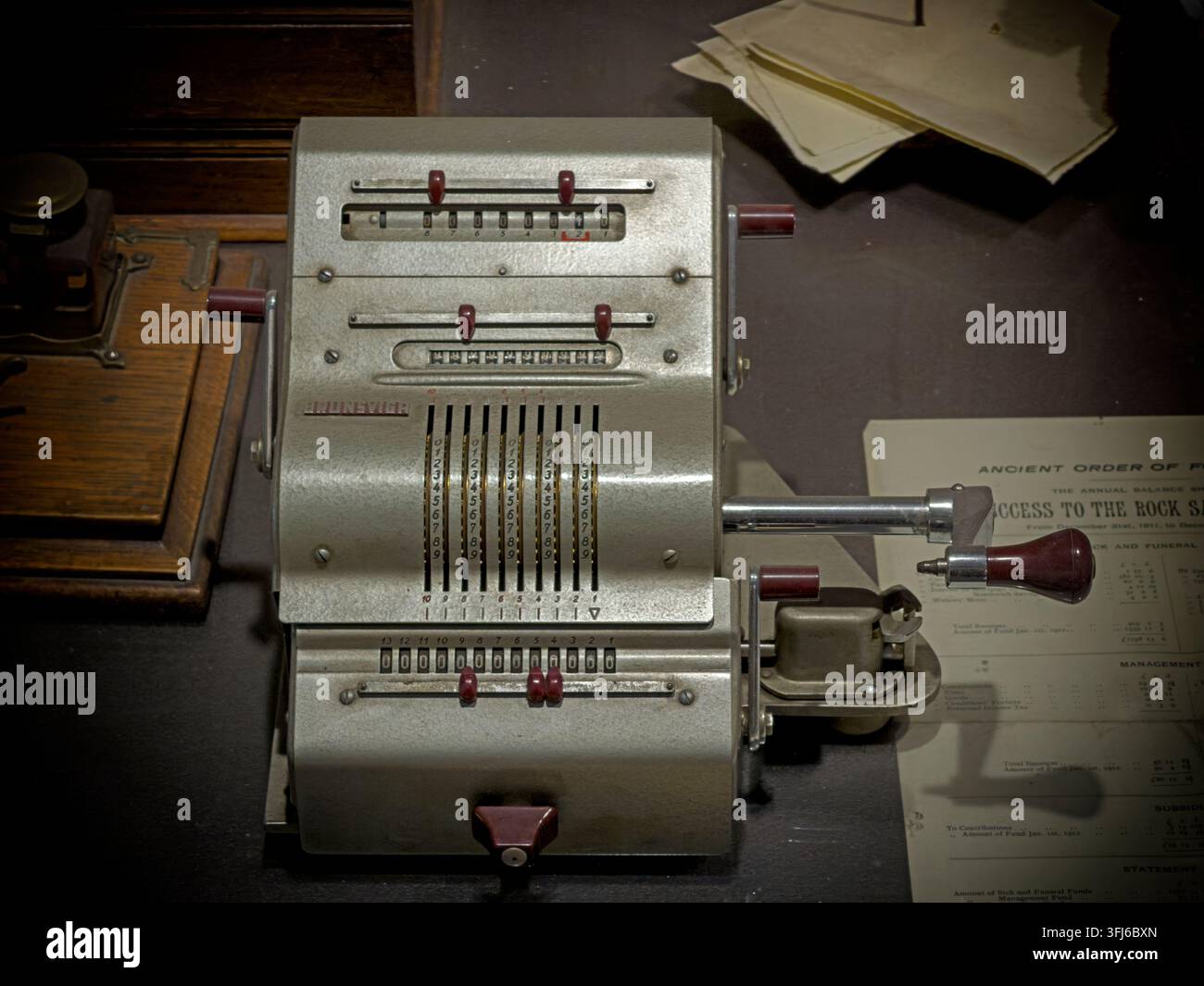 Vintage mechanical adding machine with numbered sliders and hand crank, displayed as an example of pre-electronic office calculation. Stock Photo