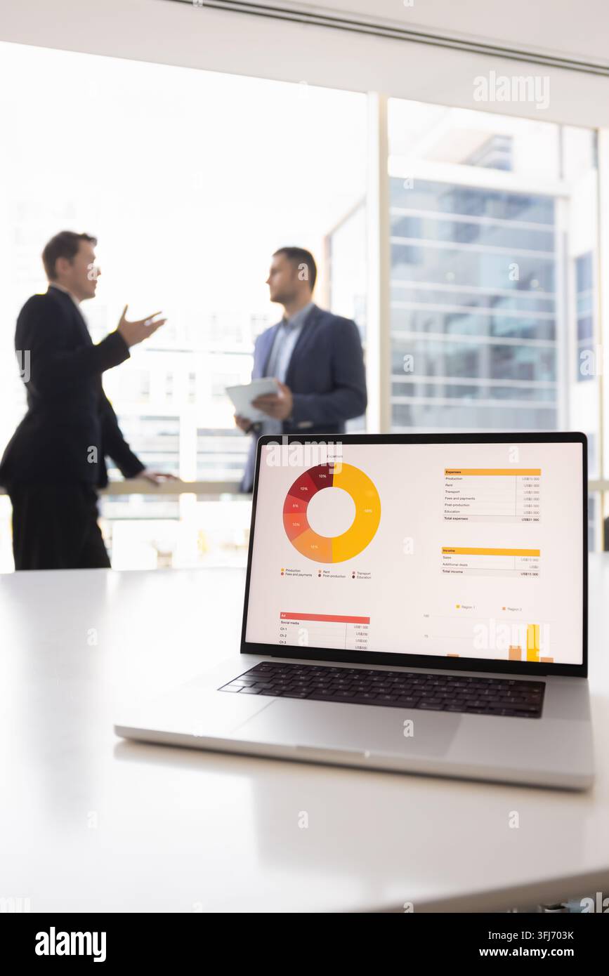 Laptop with chart and colleagues discussing data analysis in office Stock Photo