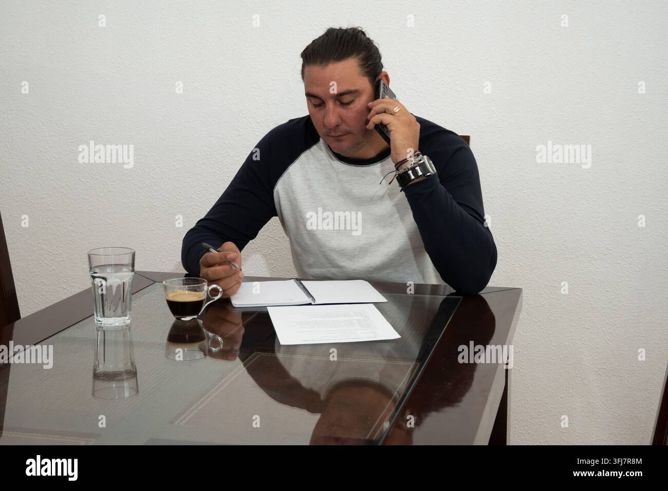 Man talking on mobile phone while writing notes at a home office table Stock Photo