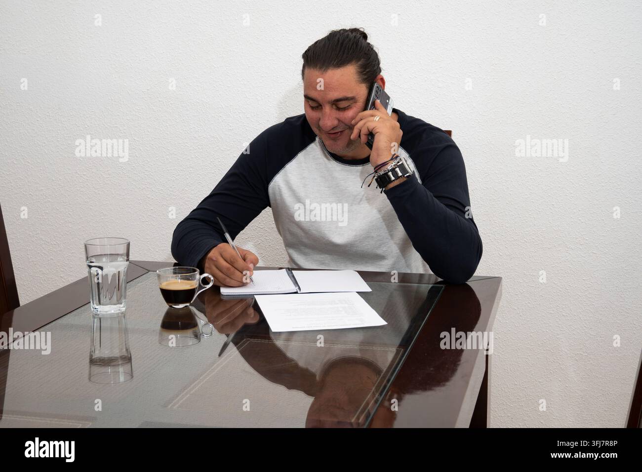 Man working from home, talking on phone and writing notes at table Stock Photo