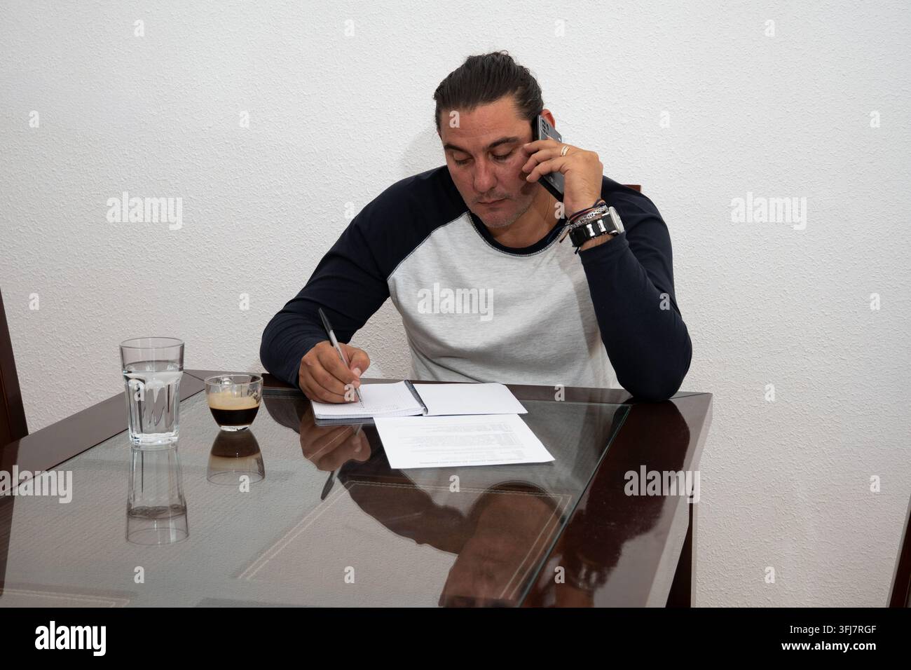 Man writing notes while talking on a mobile phone from his home office Stock Photo