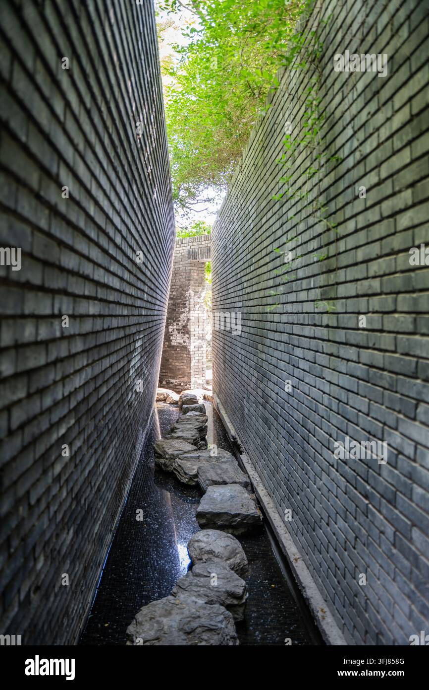 Narrow canal path between high gray brick walls Stock Photo