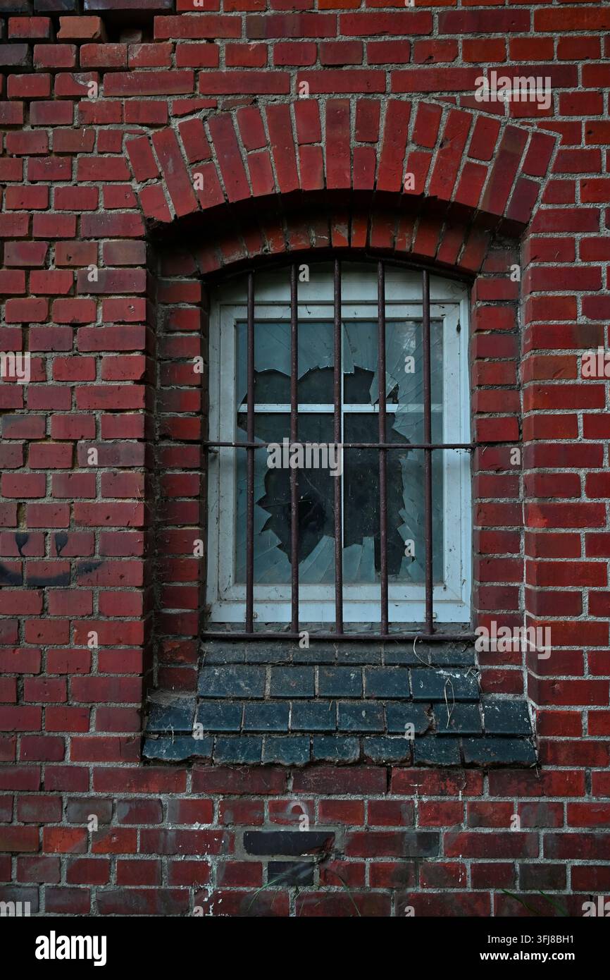 Broken window with iron bars in an old red brick wall Stock Photo
