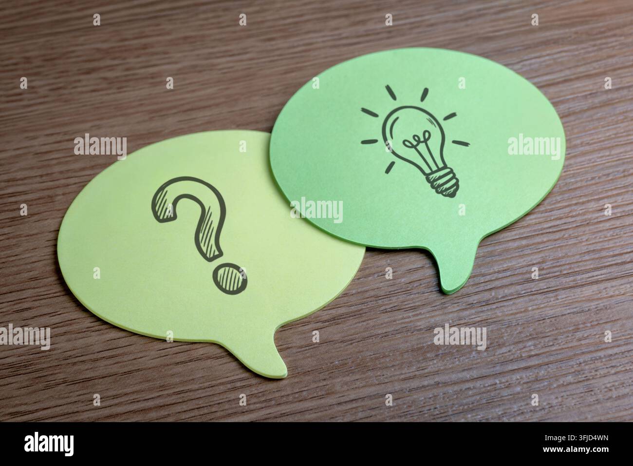Yellow and green speech bubble notes with drawn question marks and lightbulbs. Brainstorming, problem-solving, FAQ, ideation, solutions concept. Stock Photo