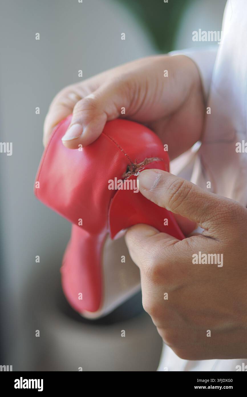 Hands fixing a torn red rubber glove in a workshop setting Stock Photo