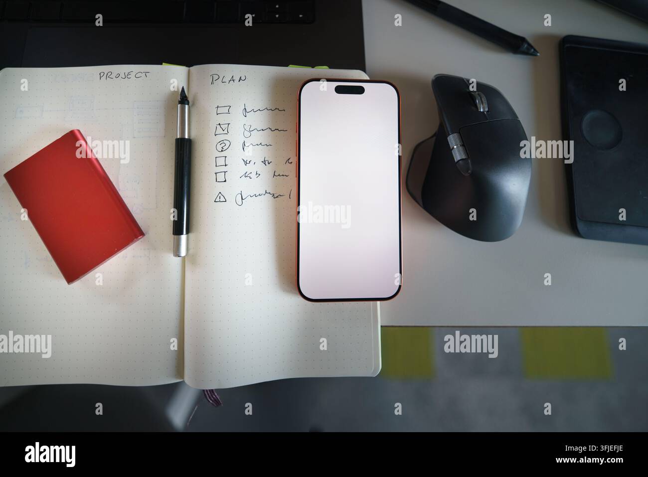 notes tech development, featuring a modern workspace with a smartphone, technical sketches in a notebook, and an ergonomic computer mouse. This techno Stock Photo
