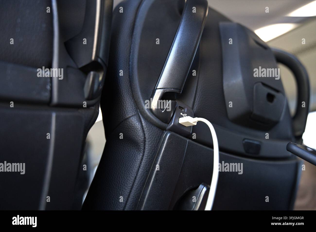 A USB port in the car seat backrest, to which a white charging cable is connected. High quality photo Stock Photo