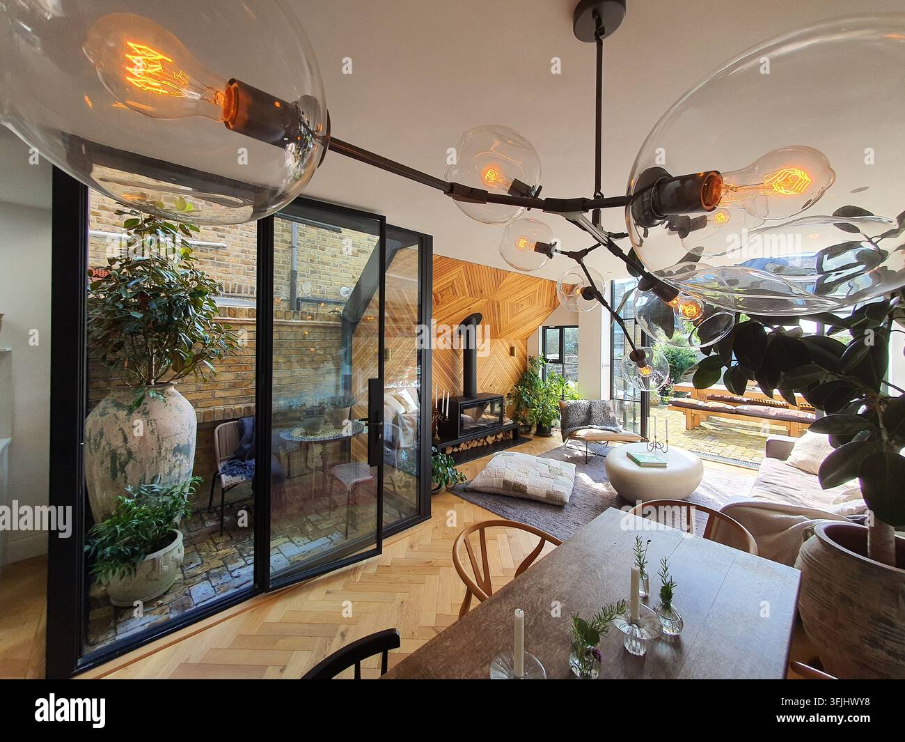 Bright, contemporary open-concept living and dining space featuring herringbone oak flooring and industrial-style pendant lighting with large glass Stock Photo