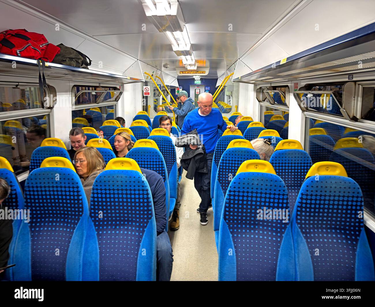 Interior of a Northern train on a Liverpool to Manchester service via Warrington, showing blue and yellow seating and passengers. Stock Photo