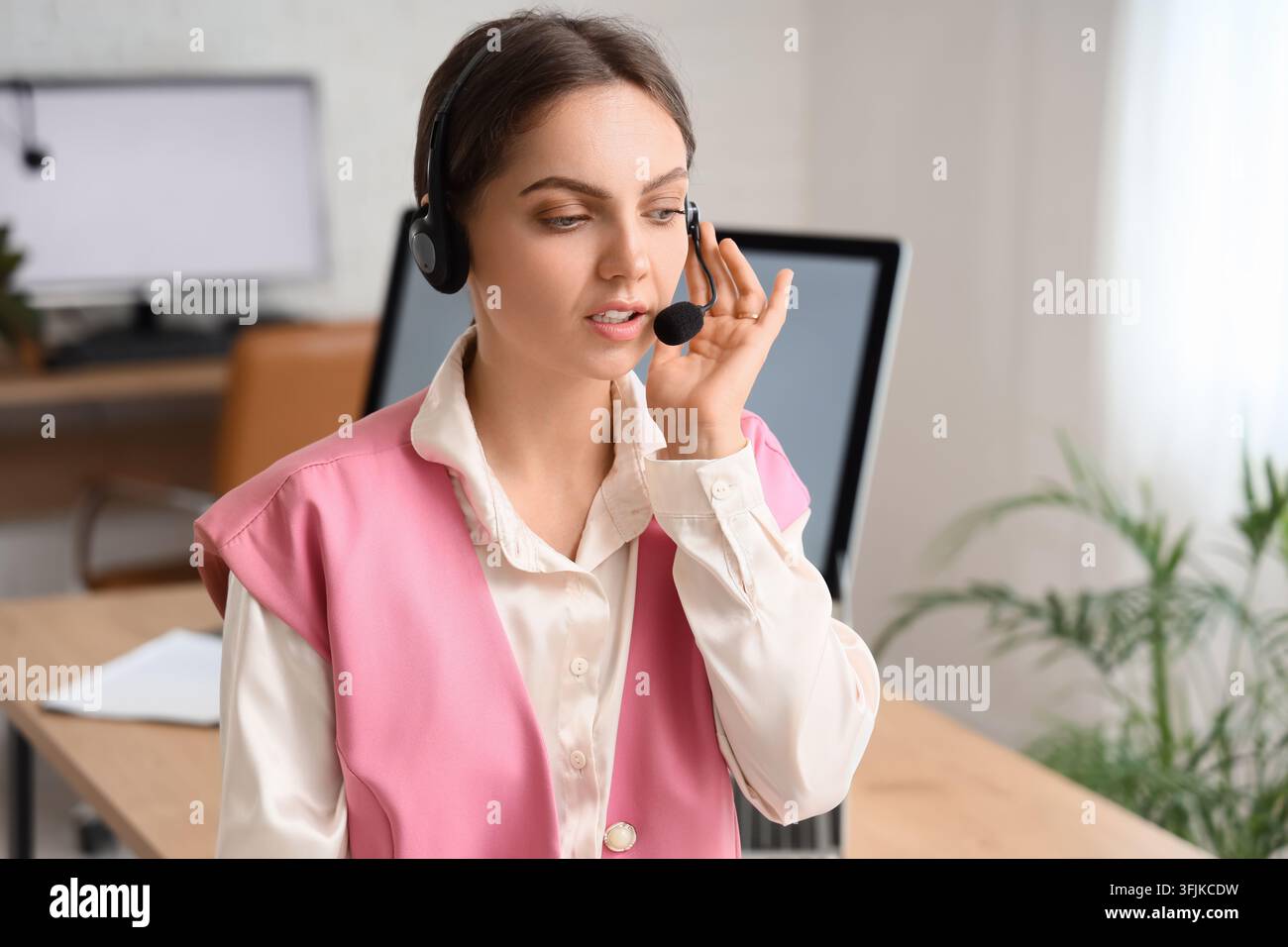 Customer support and remote assistance, young woman wearing headset working in office environment with computer and professional communication tools Stock Photo