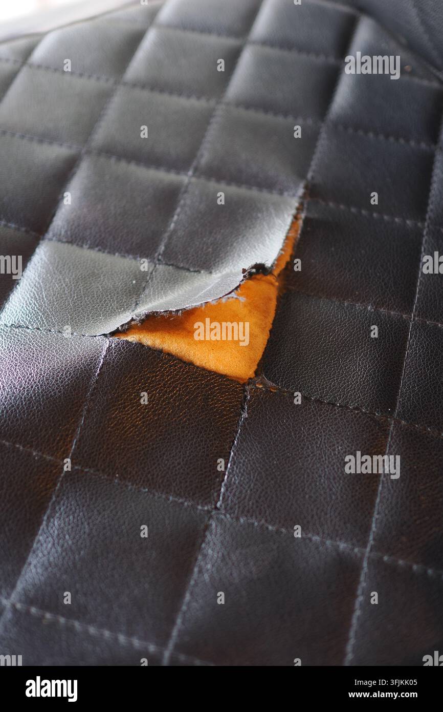 Torn black leather surface with visible orange material underneath Stock Photo