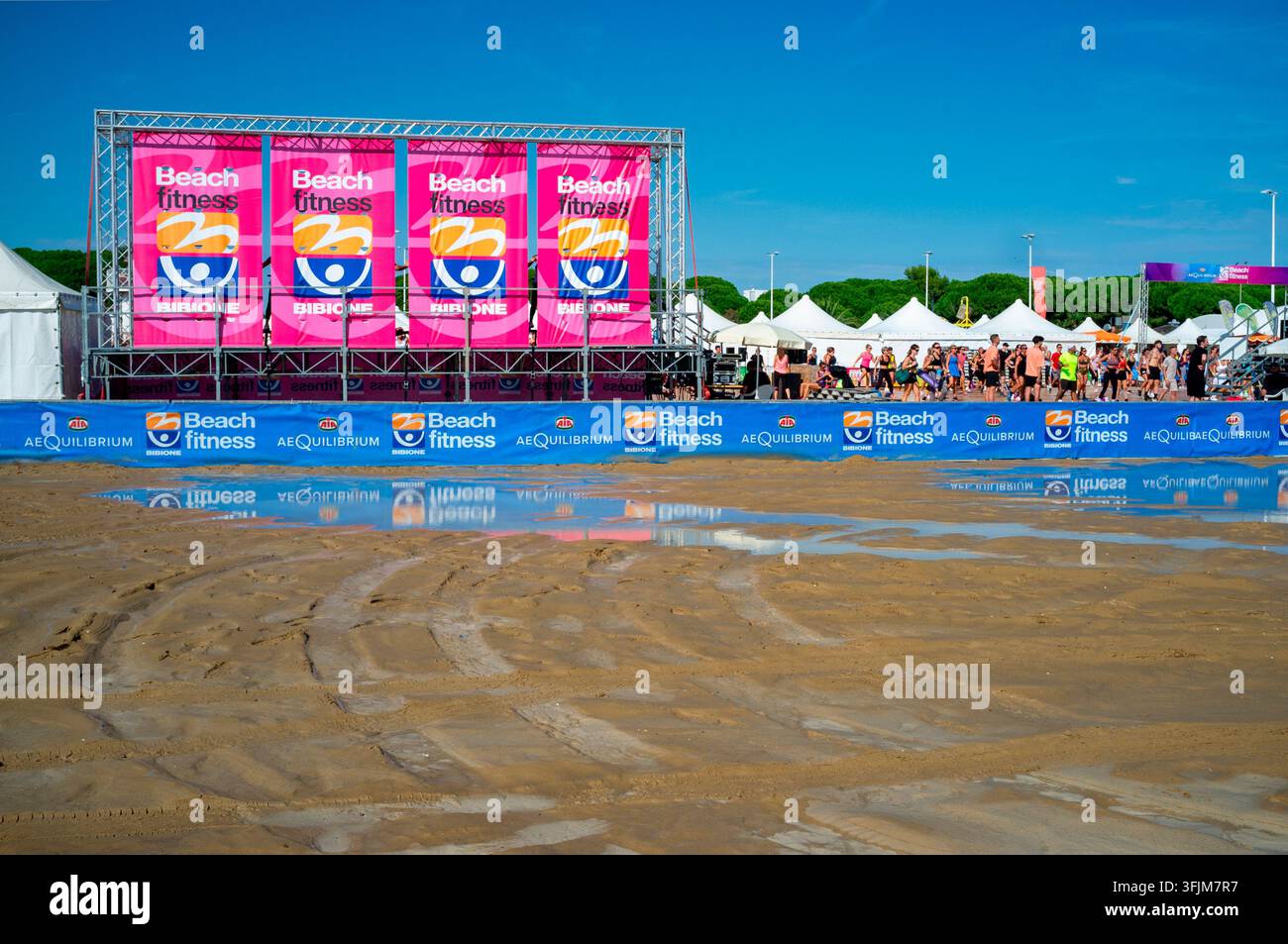 18 Sept 2026  Bibione Italy: Bibione Beach Festival, A wide-angle landscape shot of an outdoor beach fitness event stage set up on a sandy shore under Stock Photo