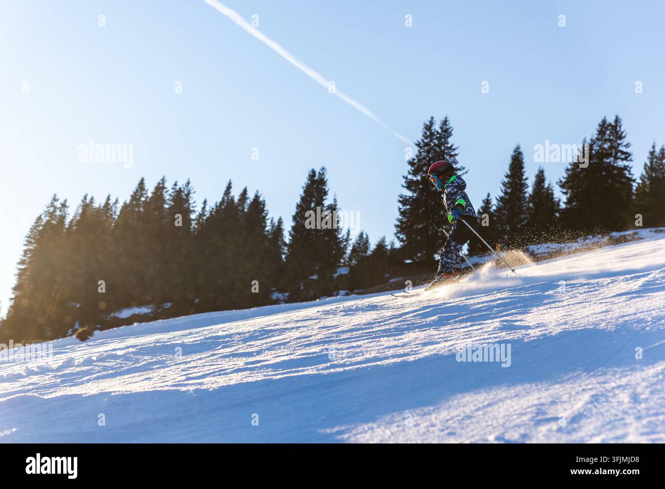 Skier kid descends snowy alpine slope at sunset, framed by mountains ...
