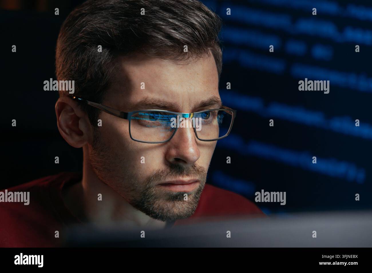Portrait of a male software engineer stares with deep focus, working on a cybersecurity or machine learning project late at night programming script reflects in his glasses. Space for text Stock Photo