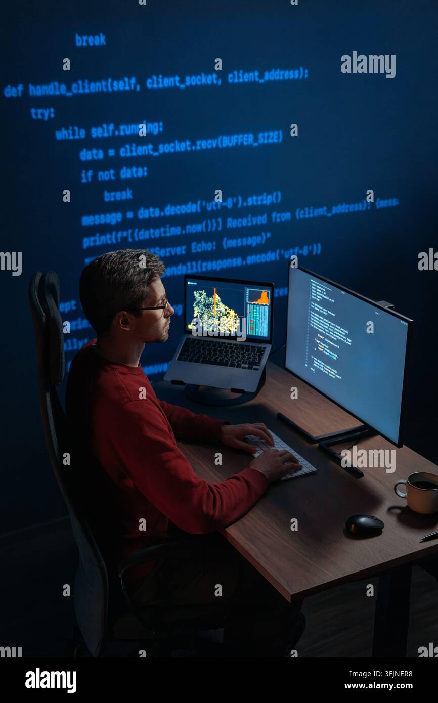 Data scientist works at night on artificial intelligence project, types on keyboard, screens displaying scripts and graphs, projection with running code on a wall behind. Copy space Stock Photo