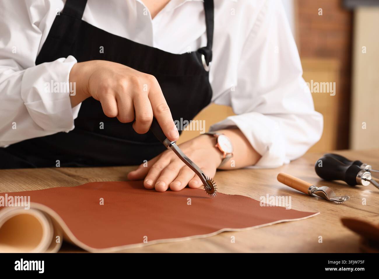 Leather craft and artisan workshop, skilled leatherworker using a tracing wheel to mark brown hide for custom handmade goods in a creative studio Stock Photo