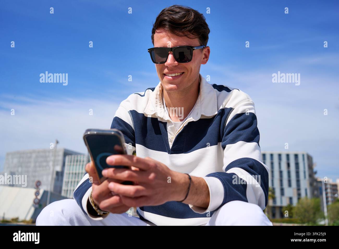 Young man smiling using smartphone in urban setting Stock Photo