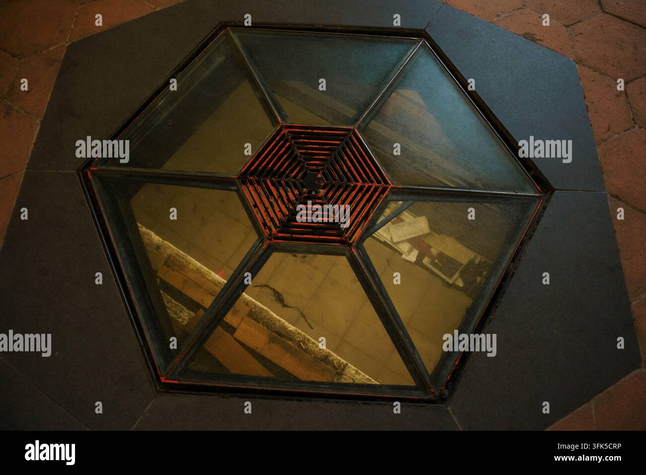 Hexagonal floor glass skylight at San Nicolo l'Arena Benedictine Monastery in Catania, Sicily, Italy, featuring a centered red metal grill, showing architectural structure and modern industrial design Stock Photo