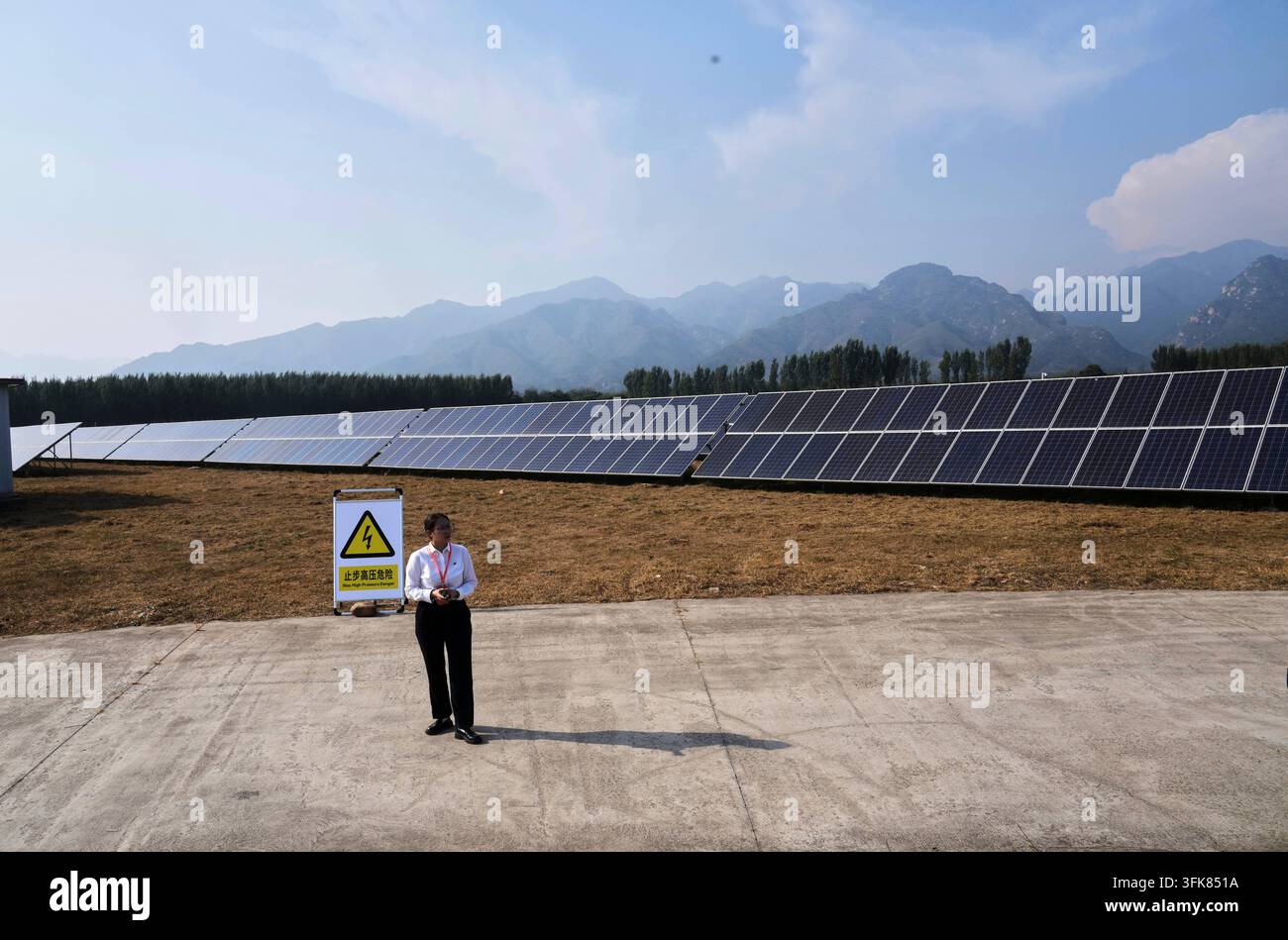 A woman stands near solar panels at a photovoltaic power station ...