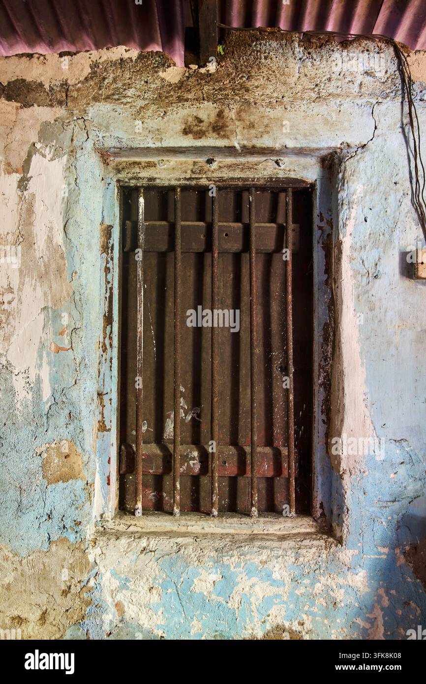 old wooden window with rusty iron bars on peeling blue wall, weathered texture and cracked paint surface, rustic architectural background Stock Photo