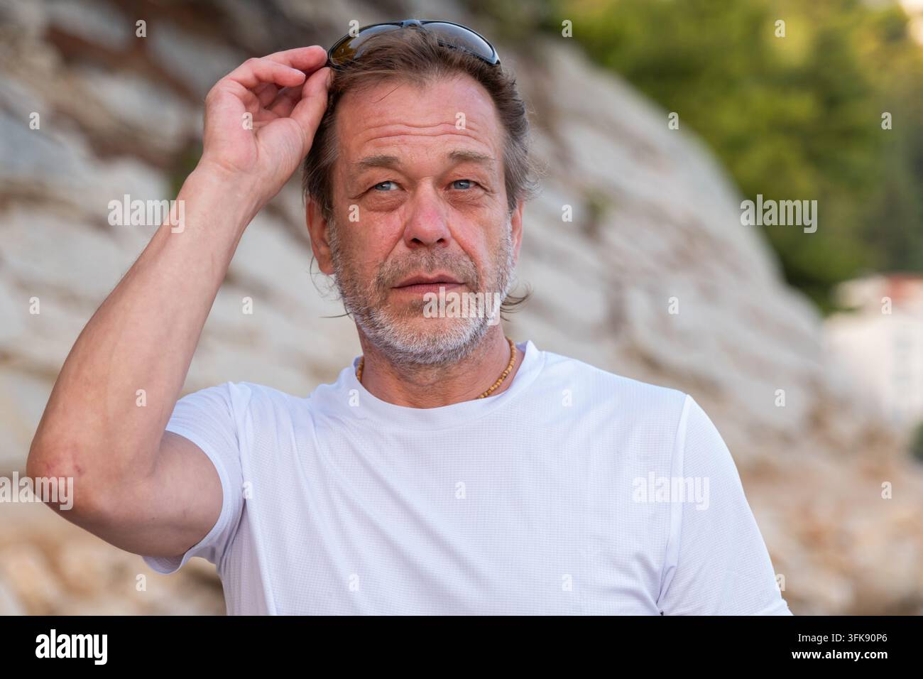 A middle aged man in a white shirt adjusts his sunglasses outdoors. Stock Photo