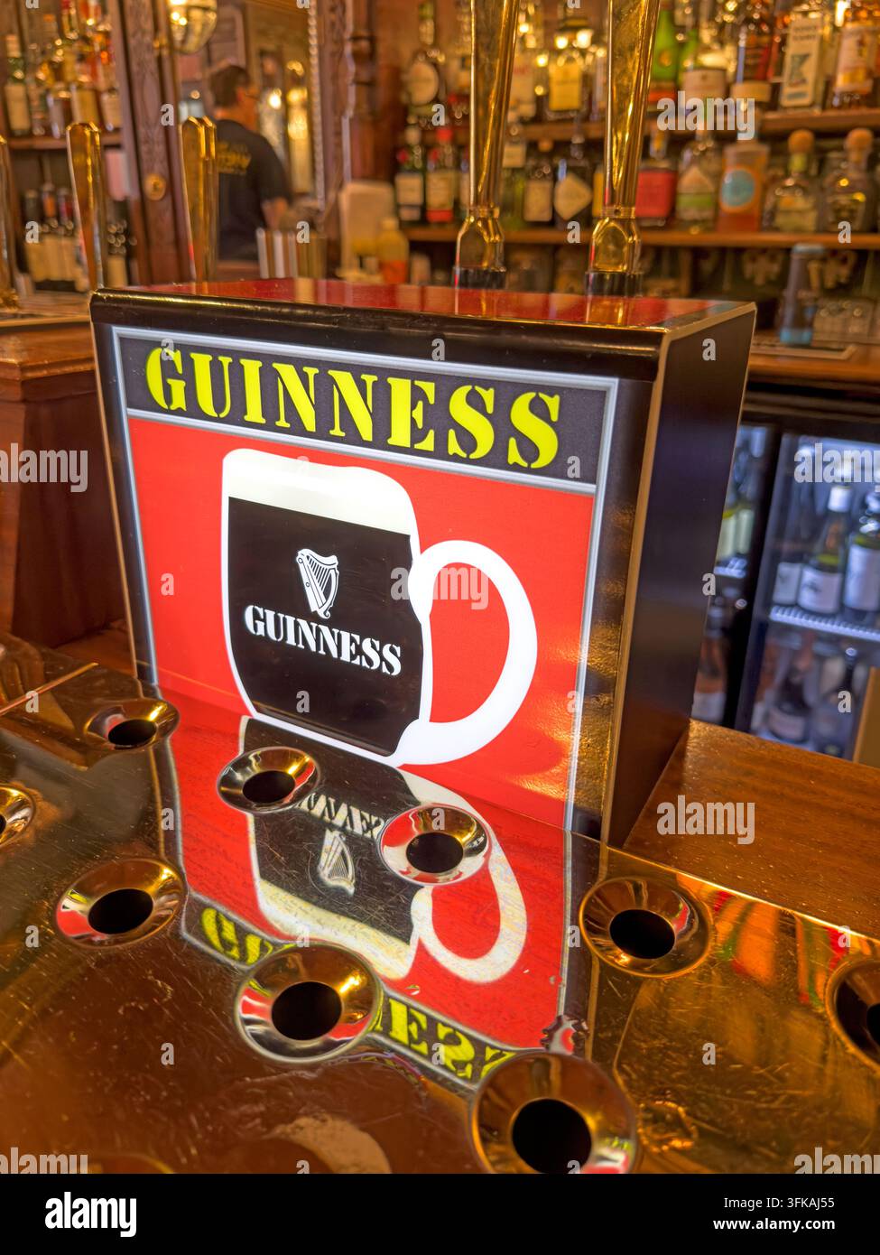 Guinness beer pump and illuminated advertising panel reflected in a polished brass bar counter inside a traditional British pub. Stock Photo