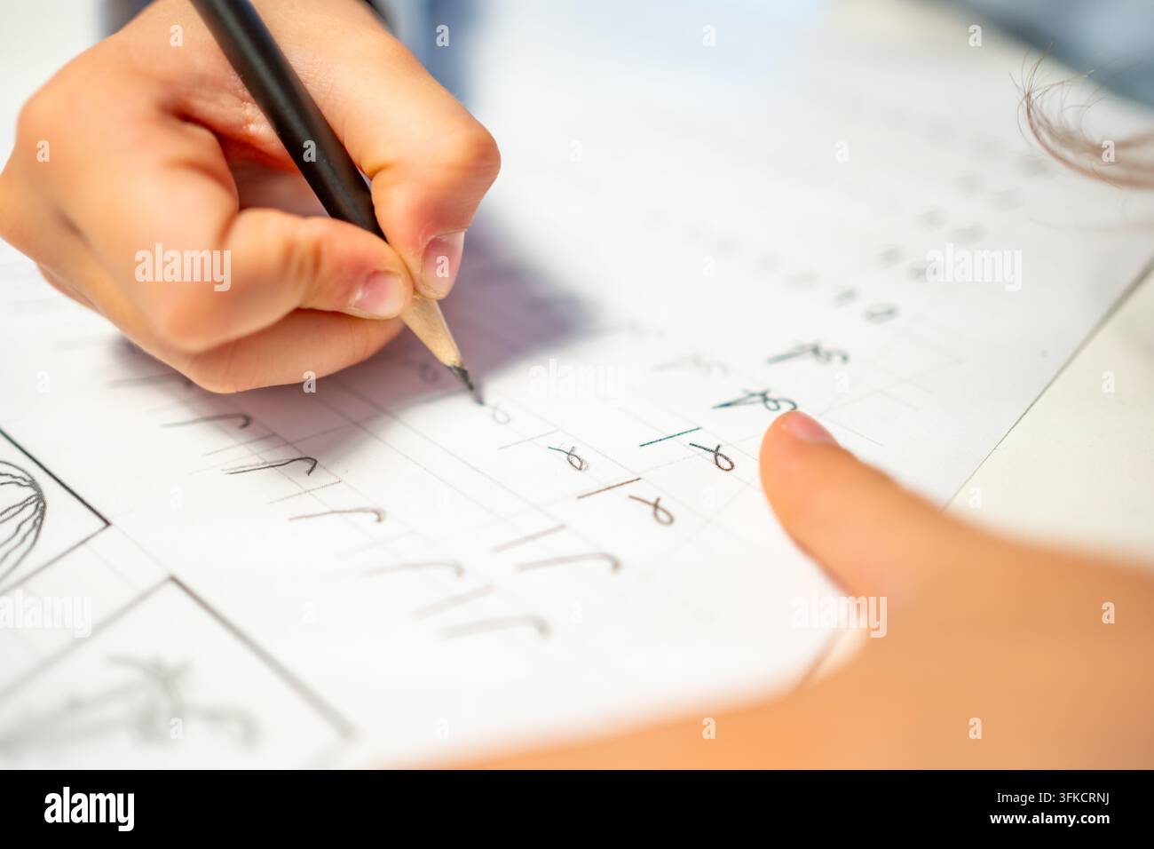 First grade student practices writing letters with pencil in workbook. Early literacy and handwriting skills develop with selective focus and shallow Stock Photo