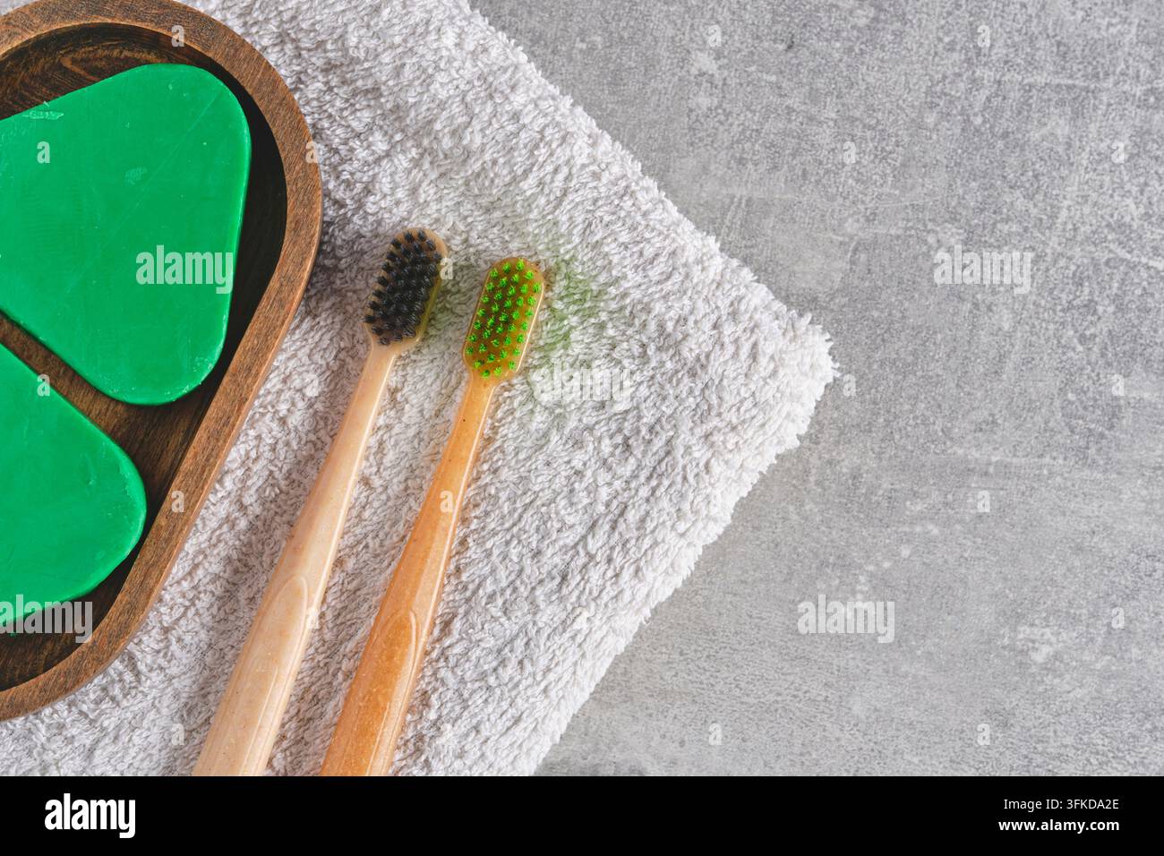 Minimalist flat lay with bamboo toothbrushes, solid shampoo, and white towel on grey surface Stock Photo
