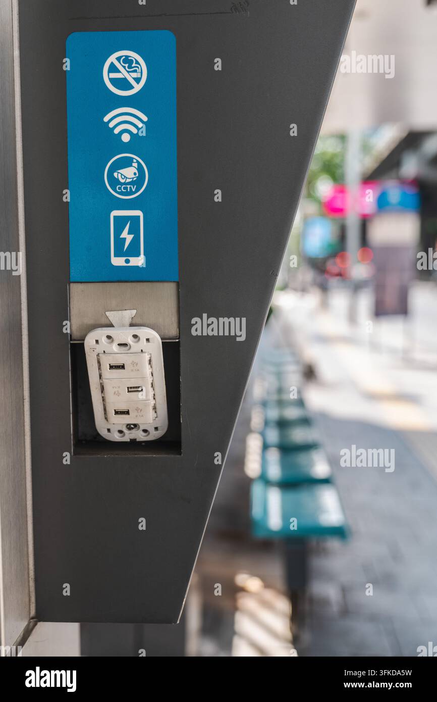 A public charging station displays Wi-Fi, CCTV, no-smoking, and battery symbols beside a softly blurred sidewalk. Stock Photo