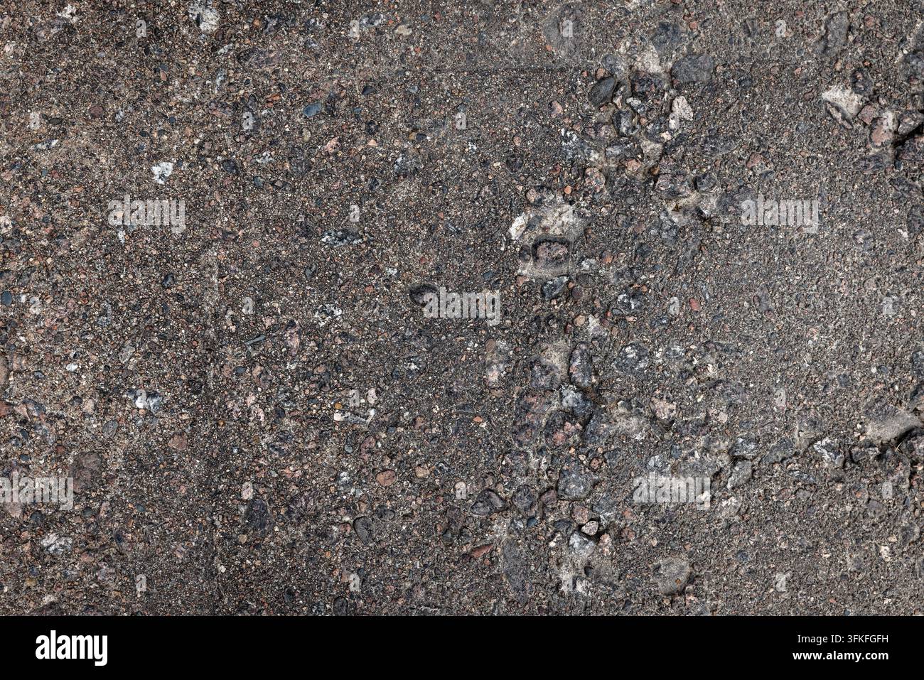 High-resolution close-up of weathered asphalt pavement showing exposed aggregate, grit, small stones and cracks. Ideal for backgrounds, texture overla Stock Photo