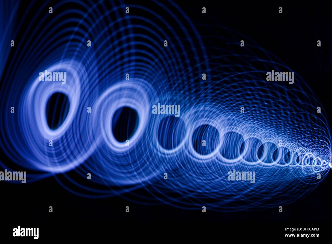 Glowing blue circular light pattern moving across a dark space. Stock Photo
