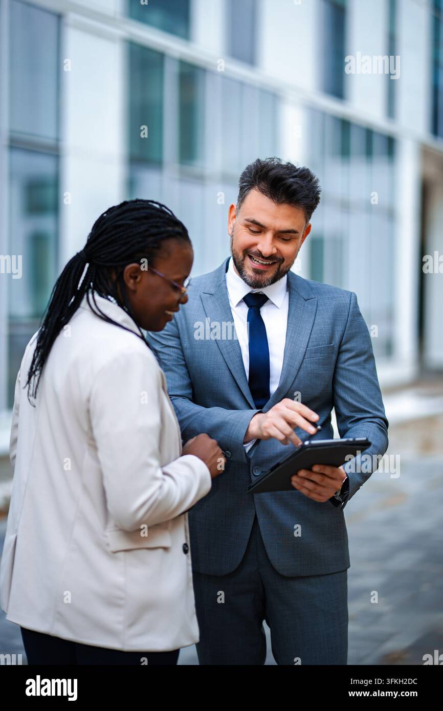 Diverse business professionals collaborating using digital tablet outdoors Stock Photo