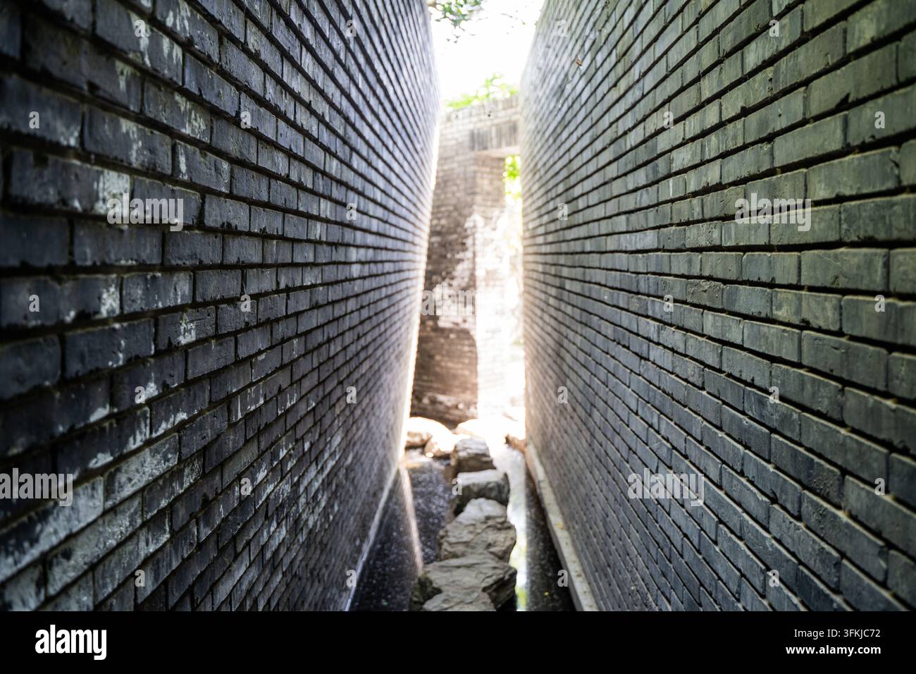 Narrow light and shadow path between high gray brick walls Stock Photo