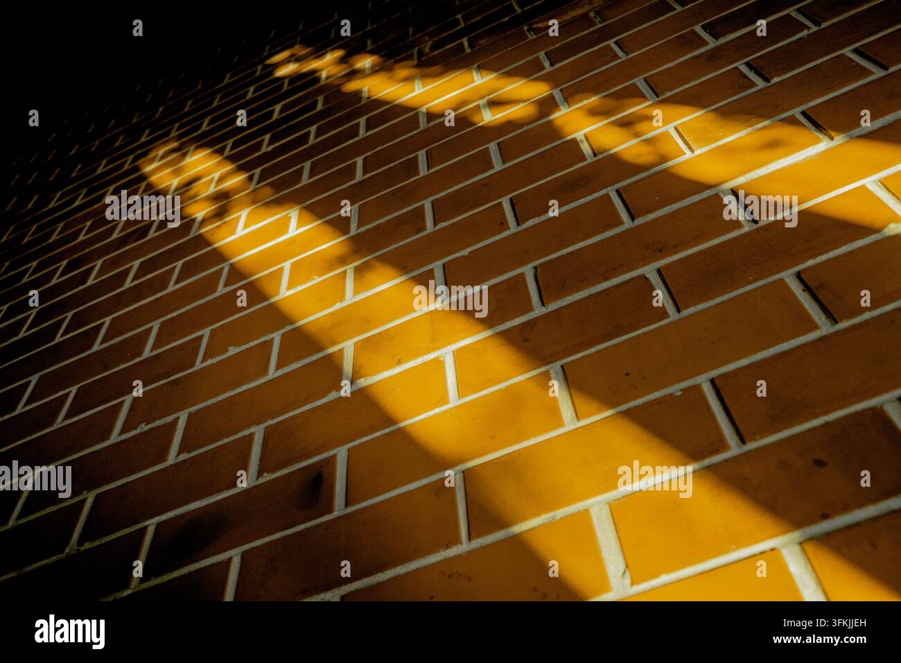 Golden sunlight casting diagonal shadows on a red brick wall Stock Photo