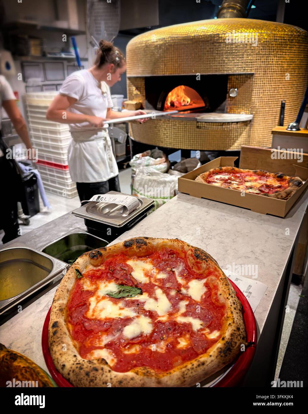 Fresh Neapolitan-style pizza beside a wood-fired oven in a busy restaurant kitchen. Stock Photo