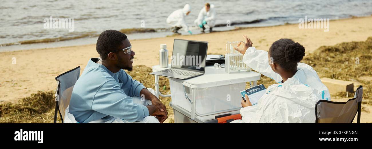 Header of Black Ecologists Analyzing Water Samples with Laptop Outdoors Stock Photo