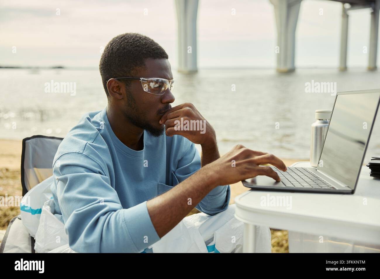 Focused Black Man Working on Laptop Outdoors by River Stock Photo