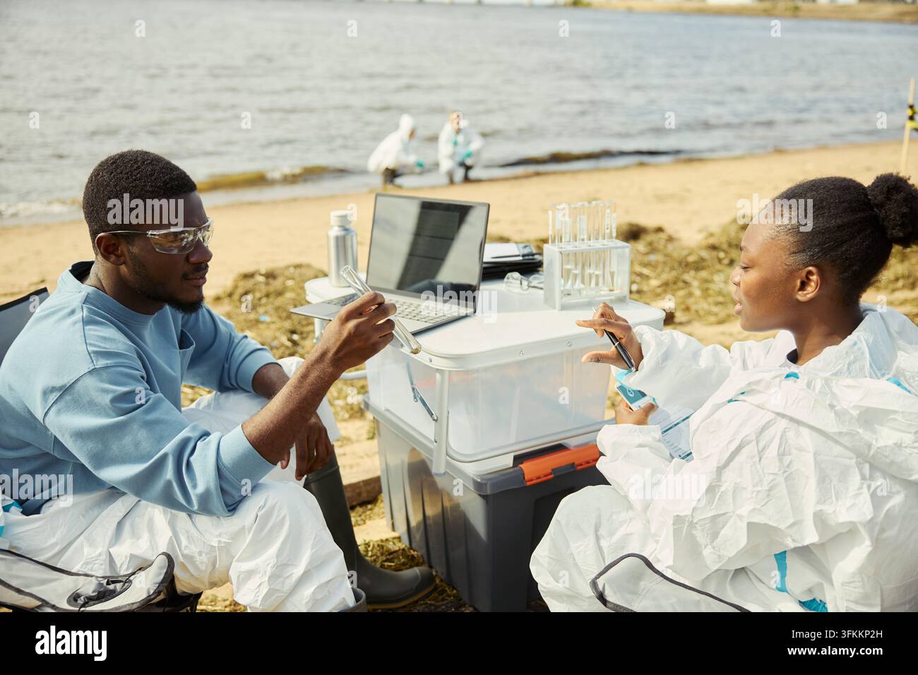 Black Ecologists Analyzing Water Samples on Shoreline Stock Photo