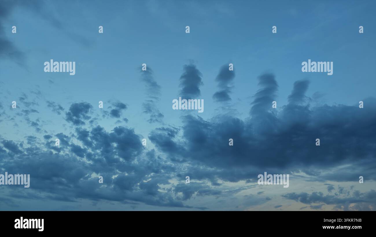 Unusual cloud formations creating vertical shapes against a light blue sky Stock Photo
