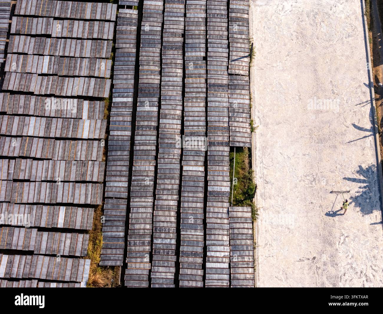Aerial view of a worker raking a large light-colored drying area beside ...
