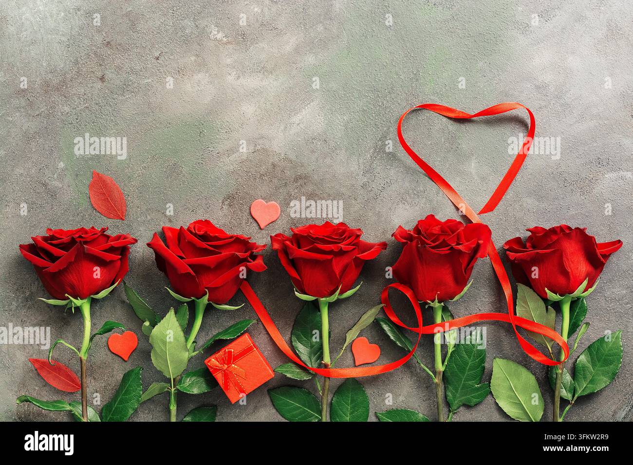Heart of red ribbon and a border of red roses on a dark rustic ...