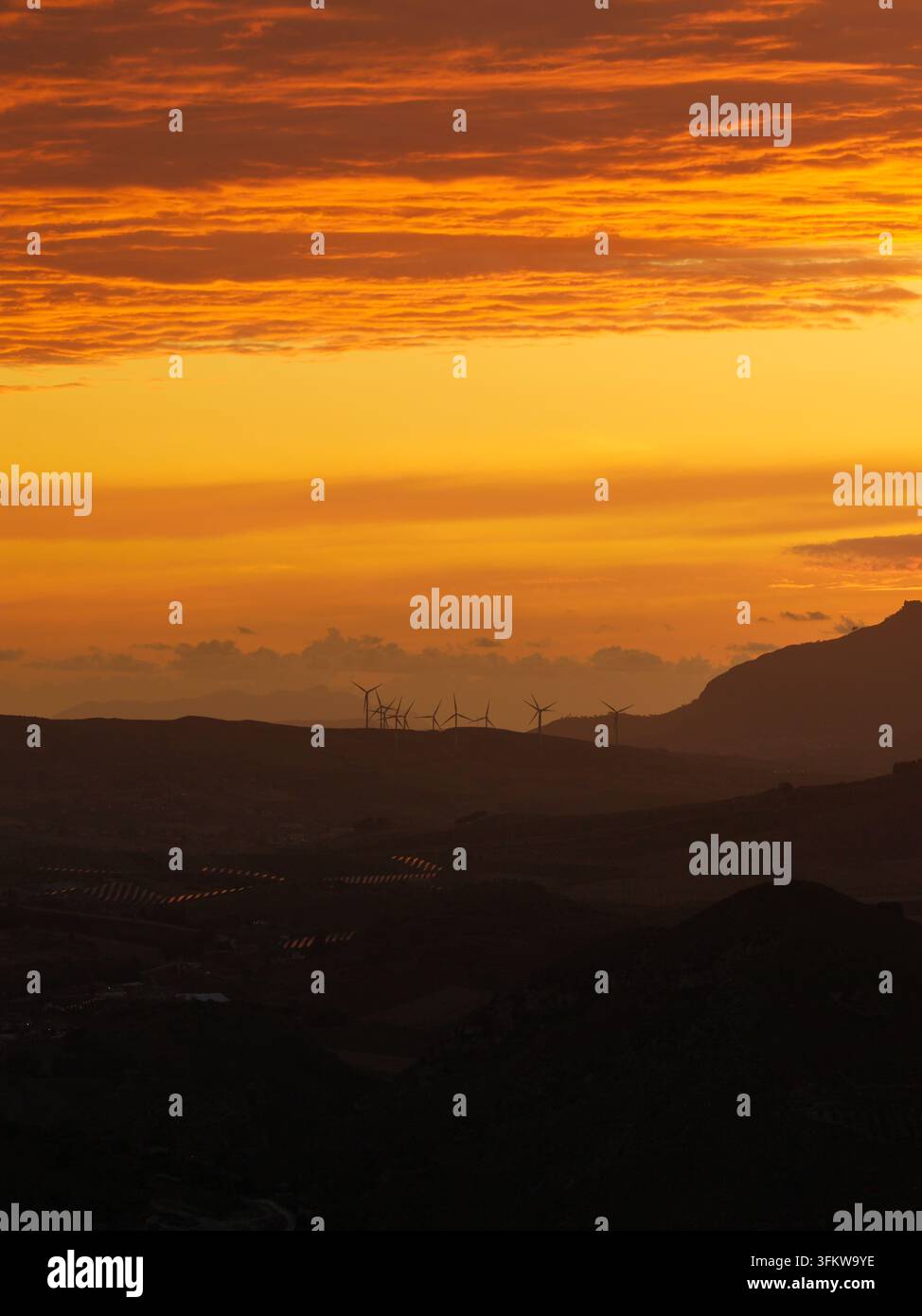 Aerial view of wind turbines silhouetted against a vibrant orange ...