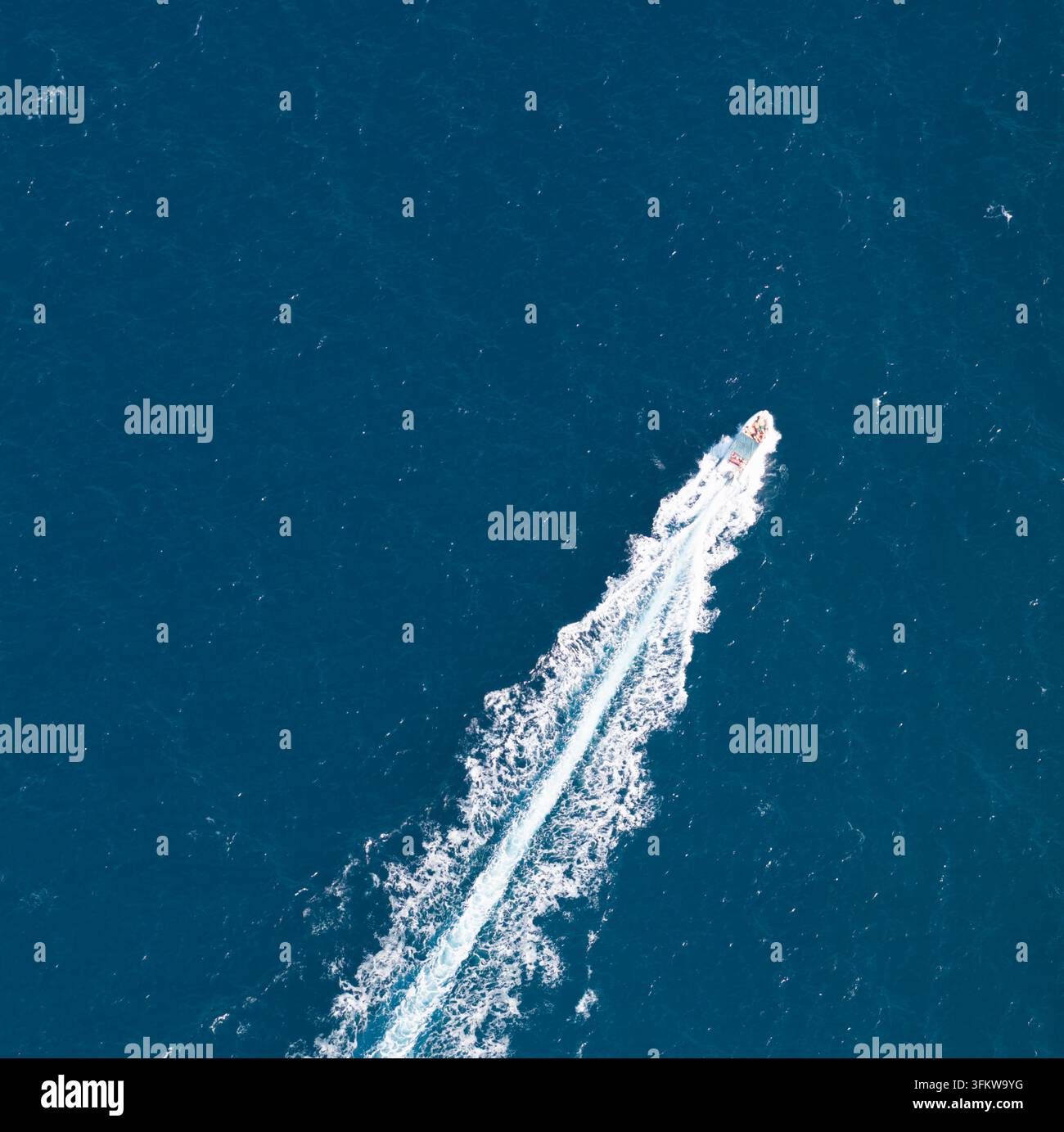 Aerial view of a small motorboat leaving a white wake in the deep blue ...